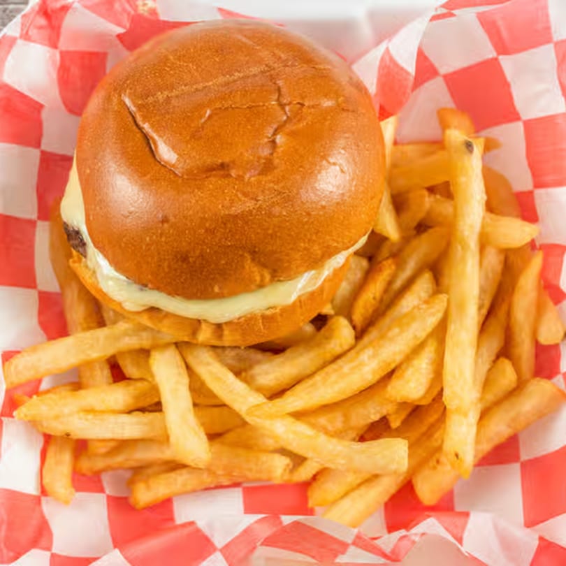 Cheeseburger with melted cheese and a side of golden french fries in a red and white checkered basket.