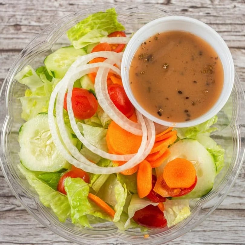 Fresh garden salad with lettuce, cucumbers, tomatoes, onions, carrots, and a side of dressing.