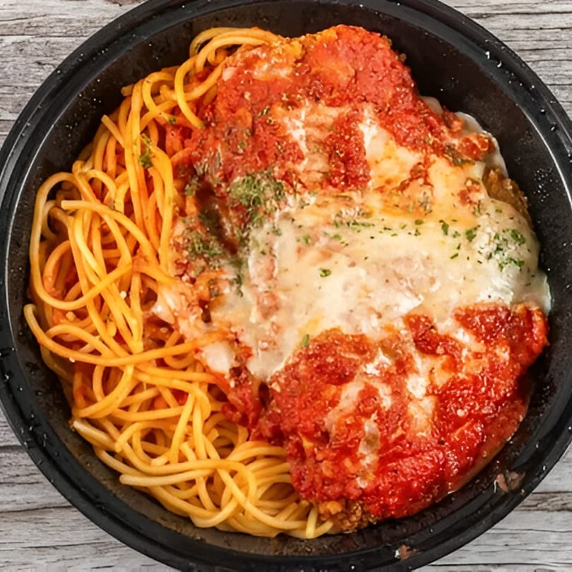 Spaghetti with chicken parmesan, topped with red sauce, melted cheese, and herbs in a black bowl.