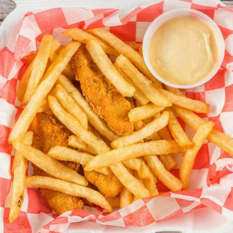 Golden french fries and chicken tenders in a red and white checkered paper basket with dipping sauce.